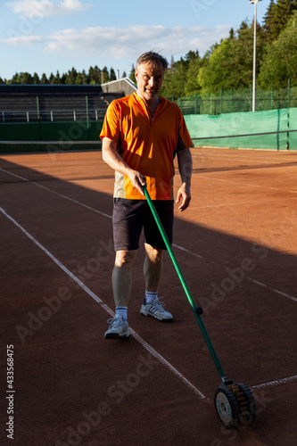 A man prepares the surface of an outdoor sand court for a match on a sunny day. Active lifestyle and professional sports. Vertical.