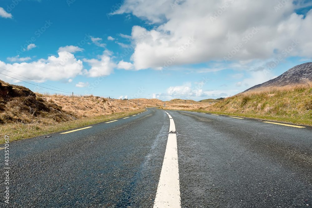 Small narrow asphalt road in Connemara, county Galway, Ireland. With beautiful nature view. Irish landscape. Cloudy sky. Low angle of view Small narrow asphalt road in Connemara, county Galway, Ireland. With beautiful nature view. Irish landscape. Cloudy sky. Low angle of view