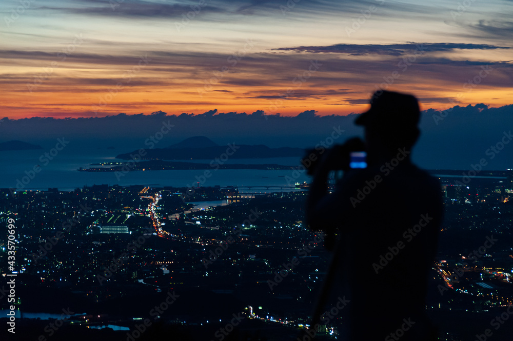 Fototapeta premium 夕焼けと街の光を撮る人