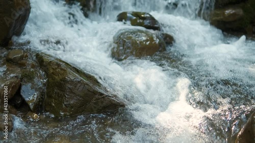 Close up of small mountain stream with clear blue water flowing between wet stones in summer forest.