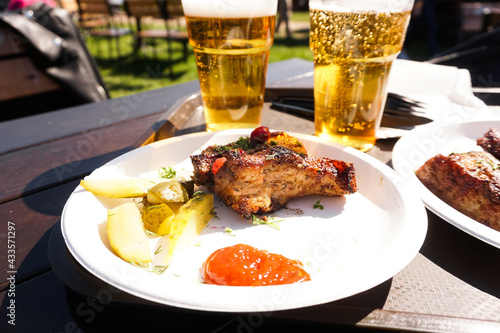 Pork ribs on a tray and light beer on wooden table background. Street food. Festival food on a sunny day photo