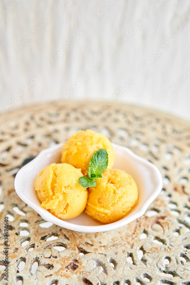 Mango ice cream with mint leaf. three balls in a white bowl on a vintage table. sorbet Mango ice cream with mint leaf. three balls in a white bowl on a vintage table. sorbet