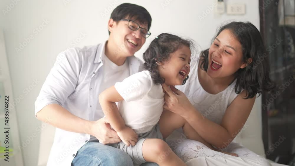 Happy Asian family relaxing at home. Smiling parents embracing and playing with little daughter on sofa in living room. Father and mother with cute child girl kid having fun weekend activity together. Happy Asian family relaxing at home. Smiling parents embracing and playing with little daughter on sofa in living room. Father and mother with cute child girl kid having fun weekend activity together.