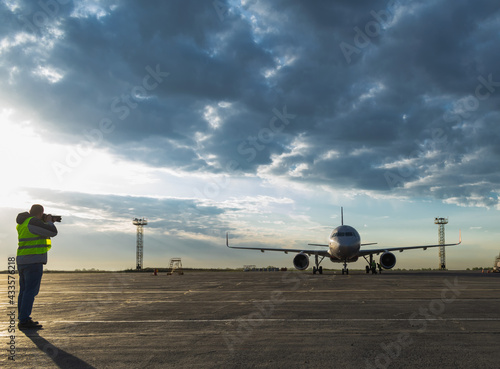 Silhouette of a spotter photographer with a camera and a telephoto lens, taking photos of an airliner.