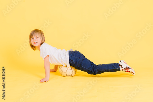 Cute boy is holding a football ball made of genuine leather isolated on a yellow background. Soccer