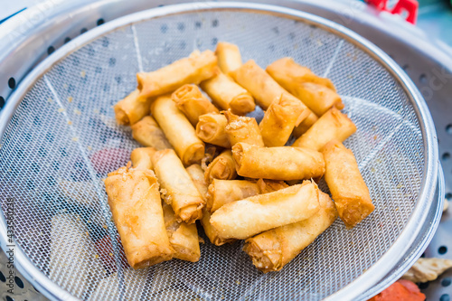 close-up of deep-fried crispy bite-sized chinese spring rolls with cabbage, carrots and green peas fillings on a black plate on a concrete table, view from above