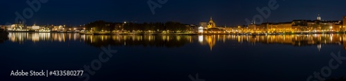 A beautiful panorama of downtown Helsinki waterfront with illuminated buildings casting reflections on the calm sea.