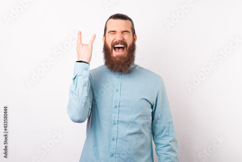 Excited bearded hipster man in blue shirt screaming and showing rock gesture © Vulp