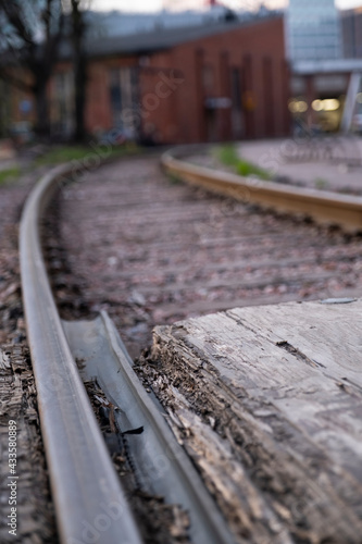 Closeup of a retro-style railway track with wooden sleepers. An old junction yard building in the background.
