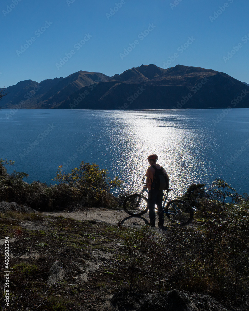 Cyclist standing with his bike enjoying the views of the Lake Wanaka on Glendhu Bay track, South Island. Vertical format