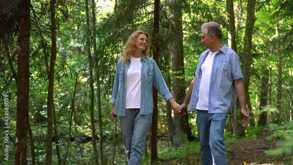 Mature couple happy man and woman of Caucasian ethnicity are walking in the park on a summer day holding each other's hands. Spending time together. High quality FullHD footage Mature couple happy man and woman of Caucasian ethnicity are walking in the park on a summer day holding each other's hands. Spending time together. High quality FullHD footage