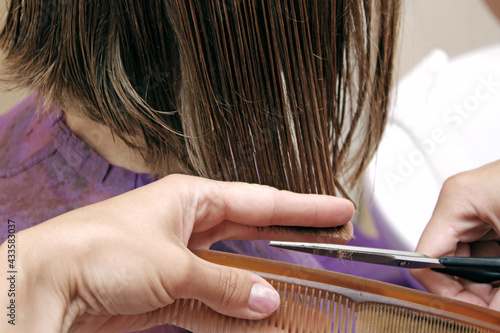 Hand of hairdresser cuts hair of woman close up in beauty salon.