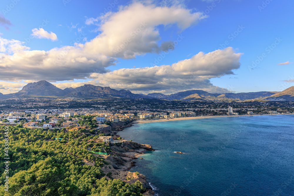 Wide view of the sea, beach, small town and mountains with blue sky and clouds.