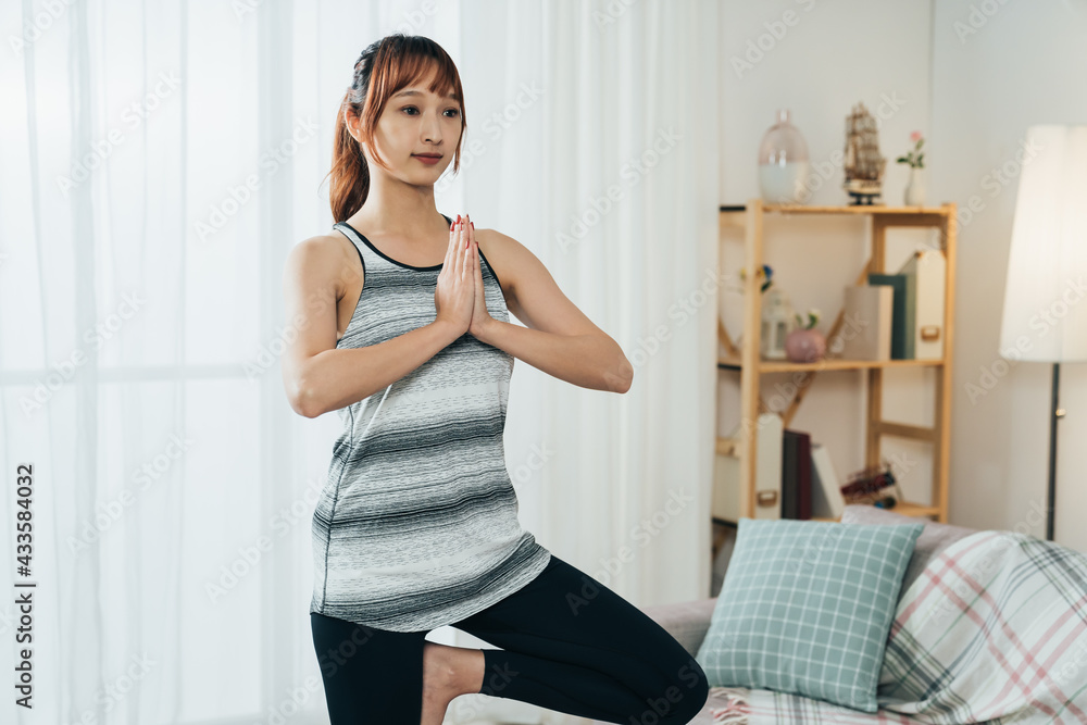 portrait fit asian girl in sportswear is practicing yoga tree pose during morning training time in the living room at home. portrait fit asian girl in sportswear is practicing yoga tree pose during morning training time in the living room at home.