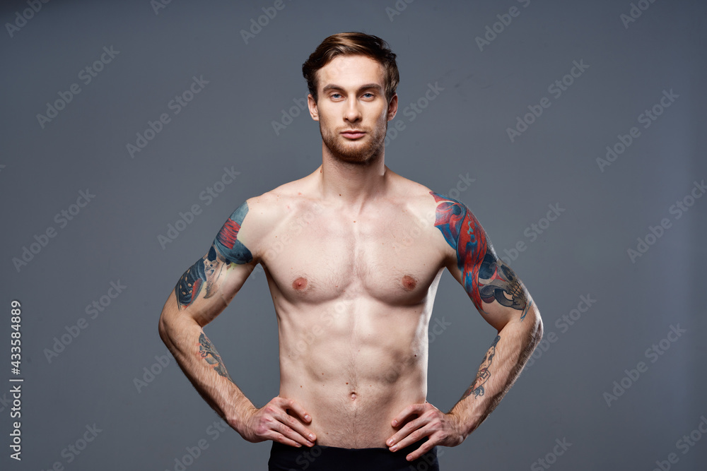 handsome man with a naked pumped-up torso tattoos on his arms holds his hands on his belt handsome man with a naked pumped-up torso tattoos on his arms holds his hands on his belt