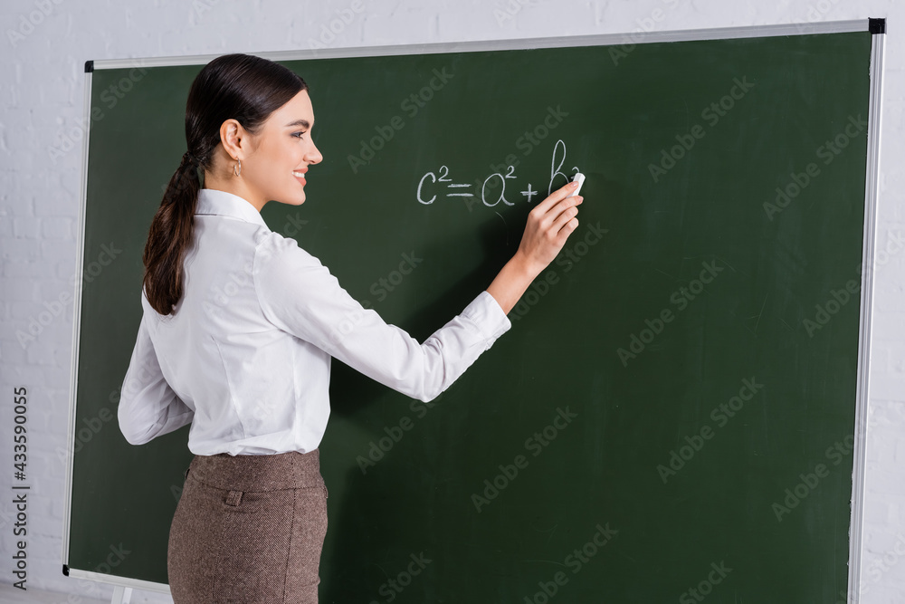 Smiling teacher writing mathematic equation on chalkboard Smiling teacher writing mathematic equation on chalkboard