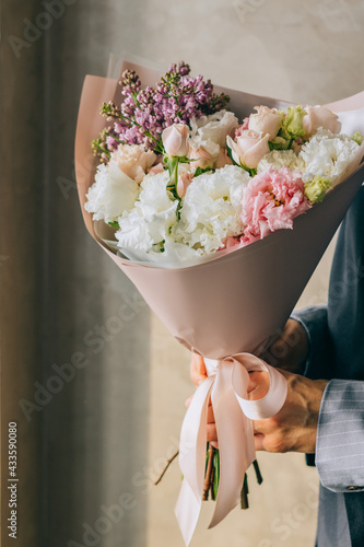 Delicate bouquet of white eustomas, pink roses and violet lilacs in beautiful packaging in the hands of a girl
