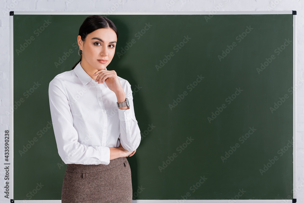 Teacher looking at camera near chalkboard Teacher looking at camera near chalkboard