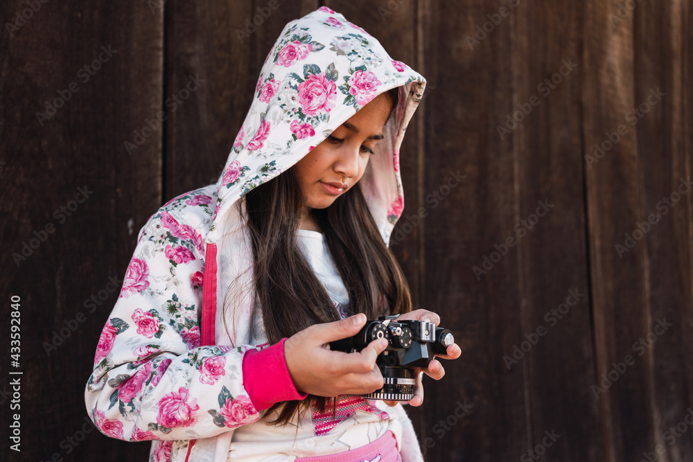 Portrait of a pretty girl holding a camera while standing against the wooden wall.