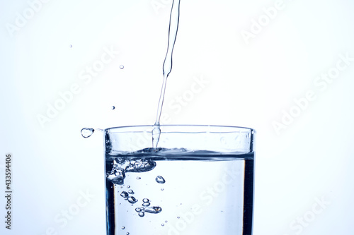 Jet of water or alcohol is pouring into a glass with splashes and bubbles, copy space