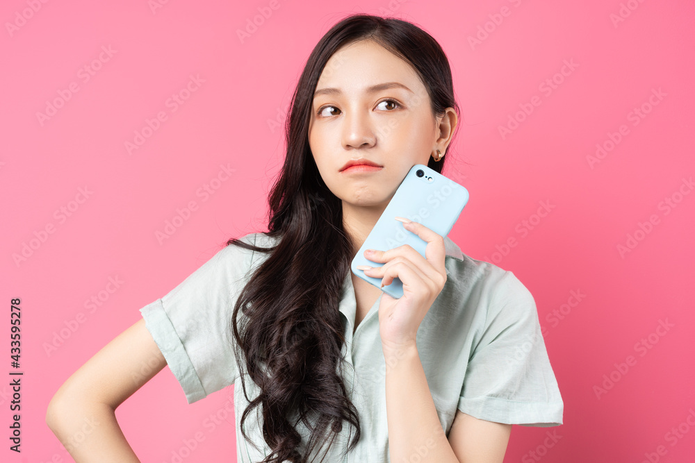 Young Asian woman holding phone in her hand with pensive look Young Asian woman holding phone in her hand with pensive look