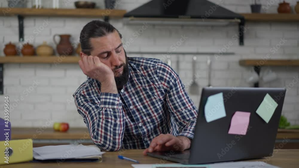 Bearded Middle Eastern man falling asleep sitting with laptop in home office. Portrait of tired overburdened handsome businessman working online in kitchen. Multitasking and burnout concept Bearded Middle Eastern man falling asleep sitting with laptop in home office. Portrait of tired overburdened handsome businessman working online in kitchen. Multitasking and burnout concept