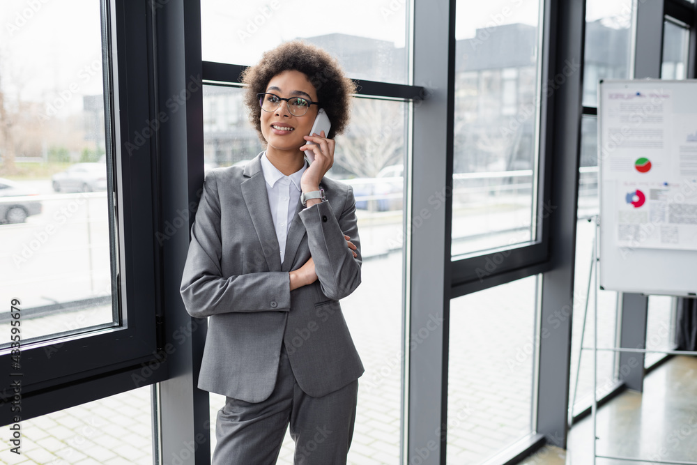 Smiling african american businesswoman talking on mobile phone near blurred flipchart Smiling african american businesswoman talking on mobile phone near blurred flipchart
