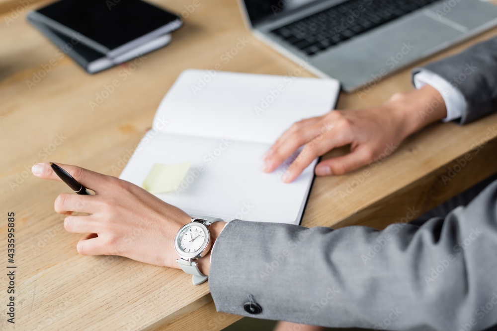 Cropped view of businesswoman holding pen near notebook on blurred background Cropped view of businesswoman holding pen near notebook on blurred background