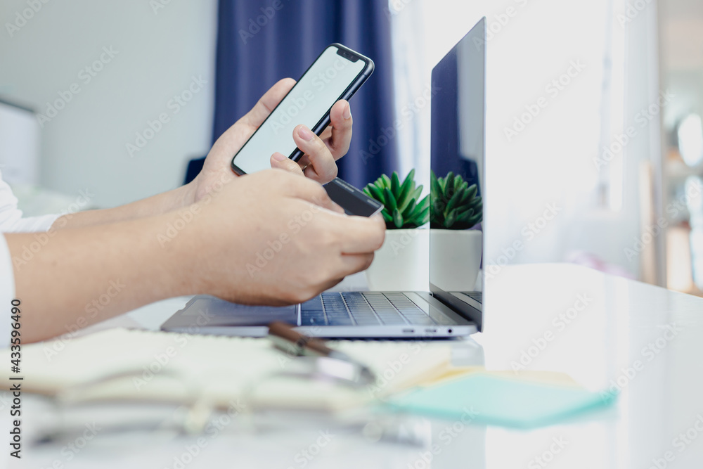 Fototapeta premium Men are using mobile phones and credit cards to pay for online purchases in their office at home.