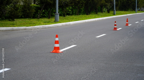 Macro shot of road traffic cones with orange and white stripes standing on street on gray asphalt during road construction works. Just painted white street lines on pedestrian crossing © Nelia2
