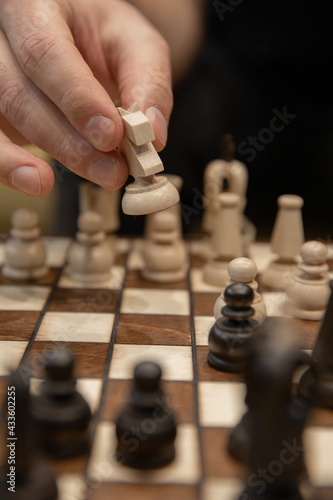 Hand taking his next step on chess game. Human hand moving wooden white knight piece on Chess board. Chess pieces in style of minimalist abstract design. unexpected business solution concept