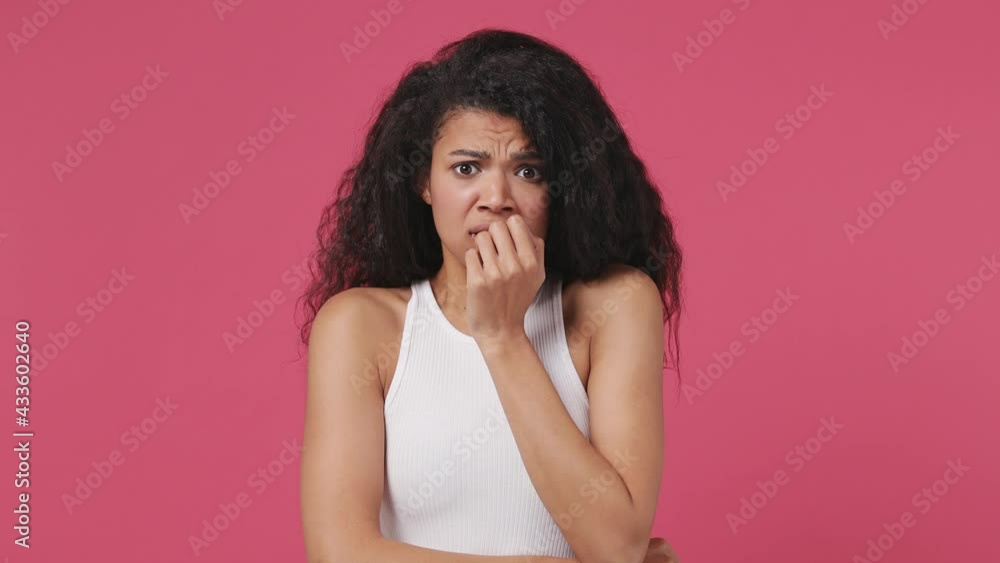 Scared shocked young african woman curly hair 20s years old wears white tank top shirt look camera cover hiding face with hands peep through fingers isolated on dark pink color wall background studio Scared shocked young african woman curly hair 20s years old wears white tank top shirt look camera cover hiding face with hands peep through fingers isolated on dark pink color wall background studio