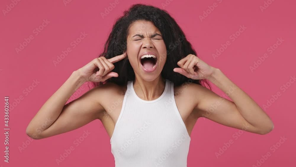 Displeased sad angry young african woman curly hair 20s years old wears white tank top shirt closed eyes cover ears do not want to listen screaming isolated on dark pink color wall background studio Displeased sad angry young african woman curly hair 20s years old wears white tank top shirt closed eyes cover ears do not want to listen screaming isolated on dark pink color wall background studio