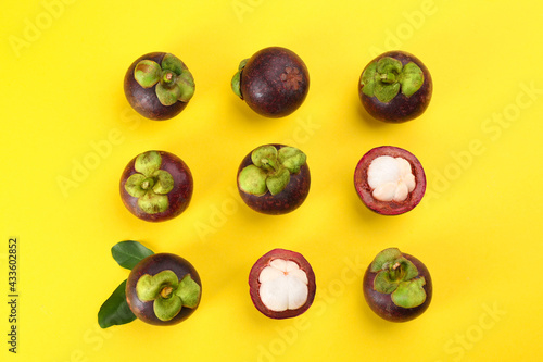 Fresh ripe mangosteen fruits with green leaves on yellow background, flat lay