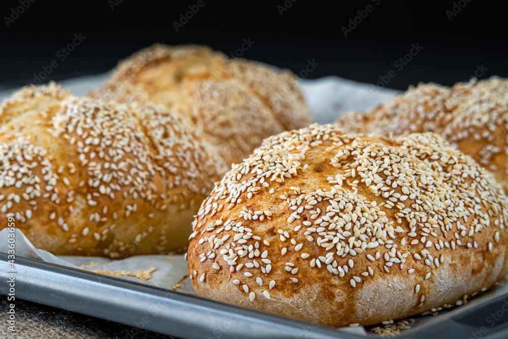 Fresh challah bread rolls hot from the oven on a baking tray. Gluten free bread buns or mini loaves with sesame seeds and golden color ready to eat. Fluffy shaped homemade bread on a dark background. Fresh challah bread rolls hot from the oven on a baking tray. Gluten free bread buns or mini loaves with sesame seeds and golden color ready to eat. Fluffy shaped homemade bread on a dark background.