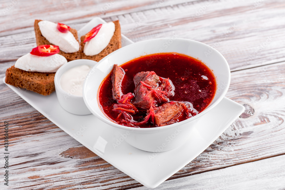 Homemade Russian, Ukrainian and Polish national soup - red borscht made of beetrot, vegetables and meat with sour cream on white wooden background
