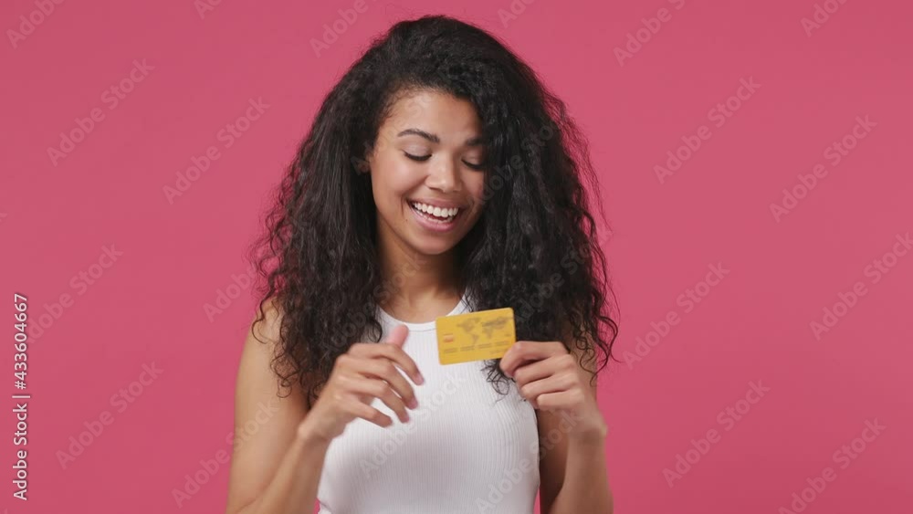 Young african woman curly hair 20s years old wears white tank top shirt pointing index finger on mockup plastic credit bank card showing thumbs up isolated on dark pink color wall background studio Young african woman curly hair 20s years old wears white tank top shirt pointing index finger on mockup plastic credit bank card showing thumbs up isolated on dark pink color wall background studio