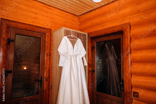 A silk dress hangs on a hanger in a wooden hotel room