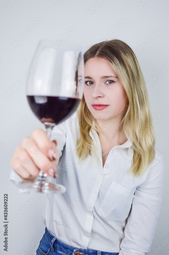 Portrait of a beautiful young blonde woman who raises a glass of red wine to appreciate its color and nuances at a wine tasting - Focus on the face Portrait of a beautiful young blonde woman who raises a glass of red wine to appreciate its color and nuances at a wine tasting - Focus on the face