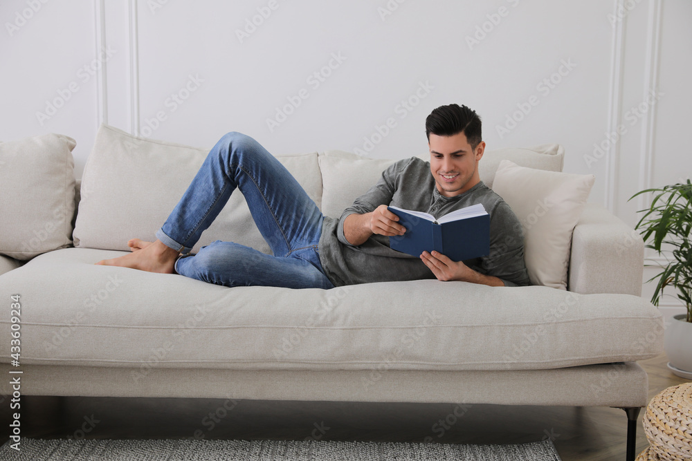 Man with book lying on comfortable sofa in living room Man with book lying on comfortable sofa in living room