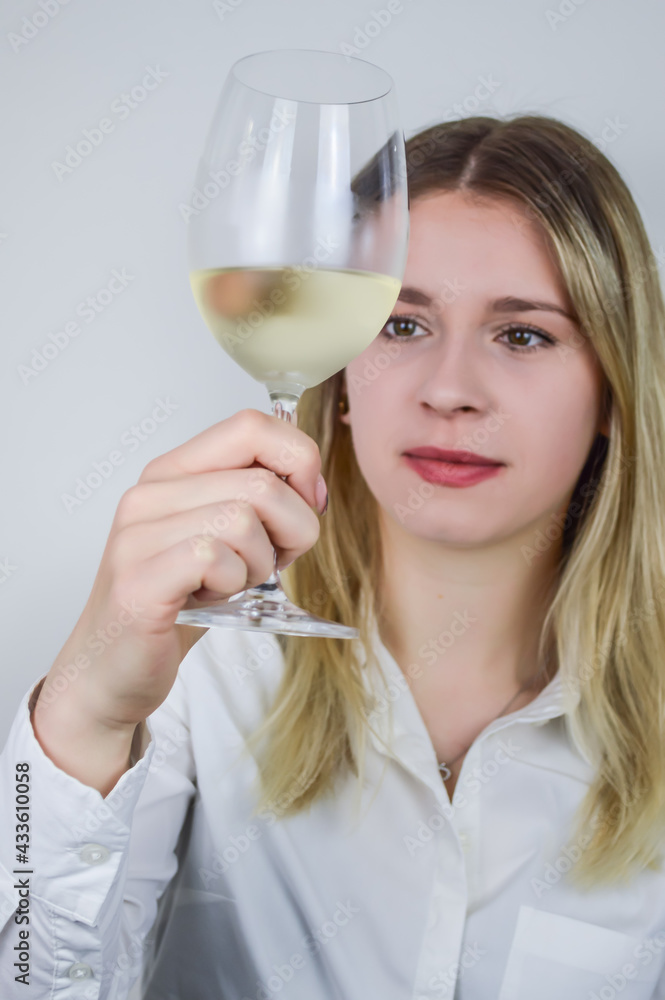 Portrait of a beautiful young blonde woman who raises a glass of white wine to appreciate its color and nuances at a wine tasting - Focus on her face Portrait of a beautiful young blonde woman who raises a glass of white wine to appreciate its color and nuances at a wine tasting - Focus on her face