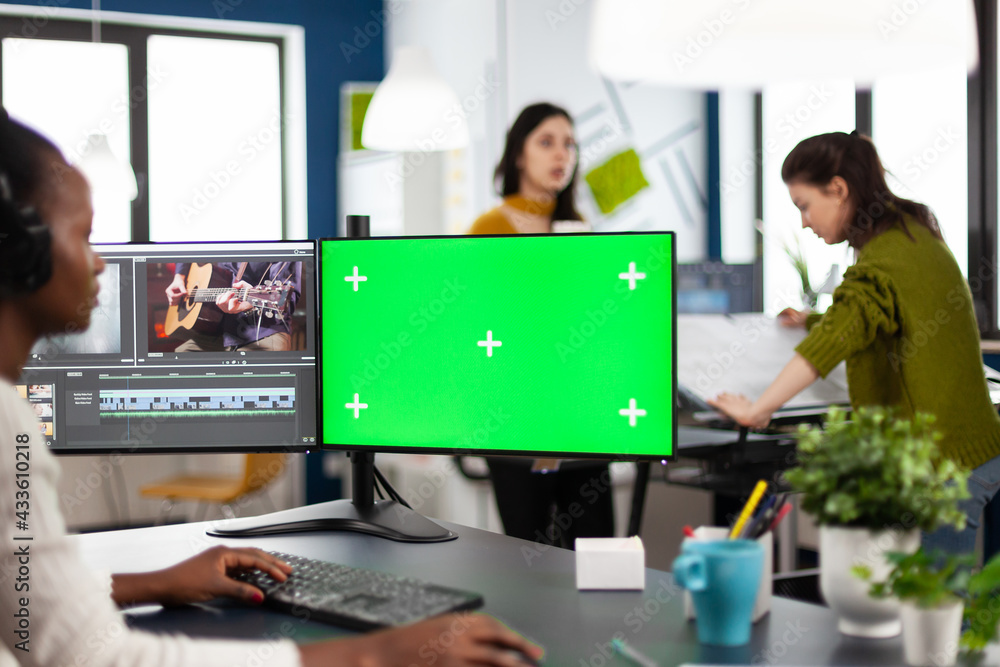 Black woman videographer employee with headphones using computer with green screen, chroma key mockup isolated display sitting in video production studio. African editor processing film montage Black woman videographer employee with headphones using computer with green screen, chroma key mockup isolated display sitting in video production studio. African editor processing film montage