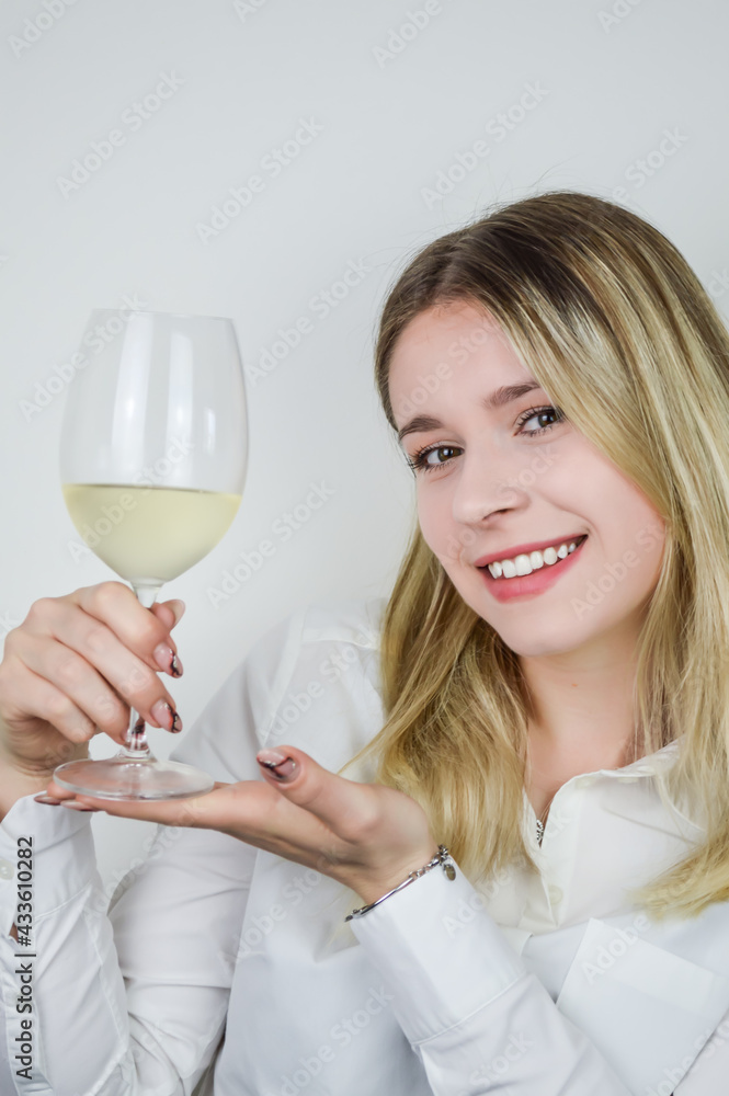 Portrait of a beautiful smiling young blonde woman holding a glass of white wine to introduce it at a wine tasting Portrait of a beautiful smiling young blonde woman holding a glass of white wine to introduce it at a wine tasting