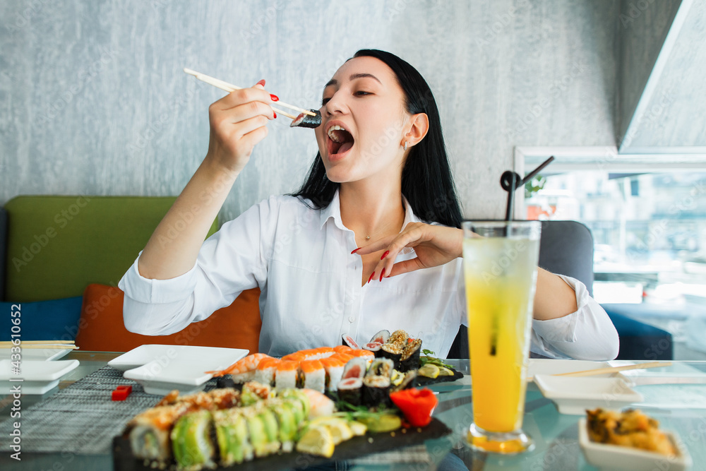 Closeup portrait of charming pleasant asian woman eating sushi and rolls, while sitting at the table at fashionable oriental restaurant Closeup portrait of charming pleasant asian woman eating sushi and rolls, while sitting at the table at fashionable oriental restaurant