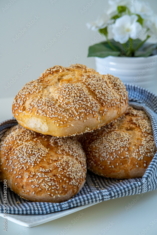 Fresh challah bread rolls hot from the oven wrapped in a towel. Gluten free bread buns or mini loaves with sesame seeds and golden color ready to eat. Fluffy homemade bread, with flowers in background