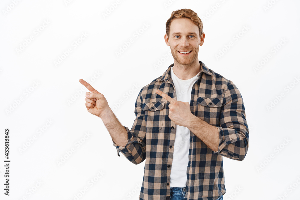 This way. Smiling redhead male model pointing fingers left and showing good advertisement, promotional offer, standing happy and confident against white background This way. Smiling redhead male model pointing fingers left and showing good advertisement, promotional offer, standing happy and confident against white background