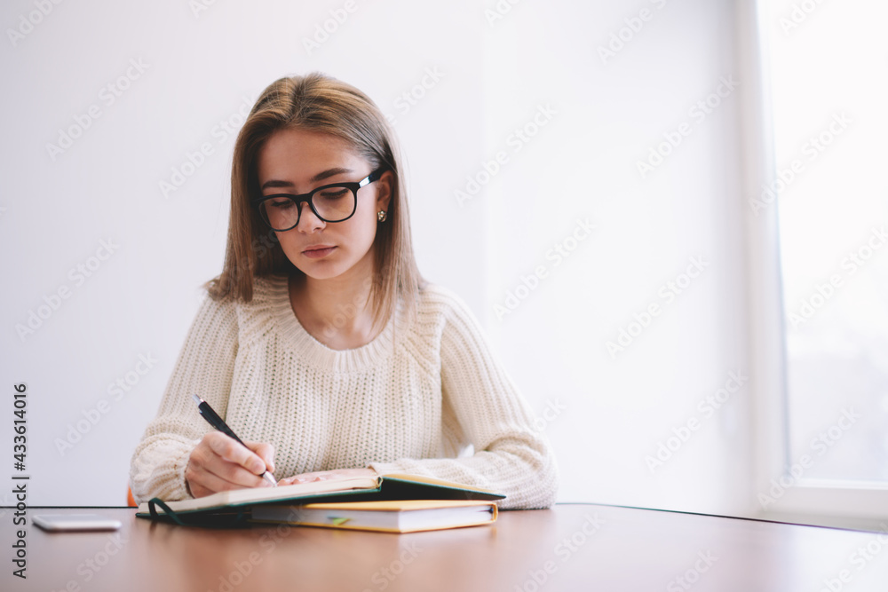 Thoughtful woman writing in notepad during exam preparation