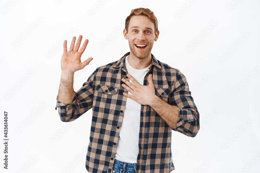 Image of smiling redhead man holding one raised and another hand on heart, introduce himself, my name is nice to meet you gesture, saying hello, standing friendly and happy against white background Image of smiling redhead man holding one raised and another hand on heart, introduce himself, my name is nice to meet you gesture, saying hello, standing friendly and happy against white background