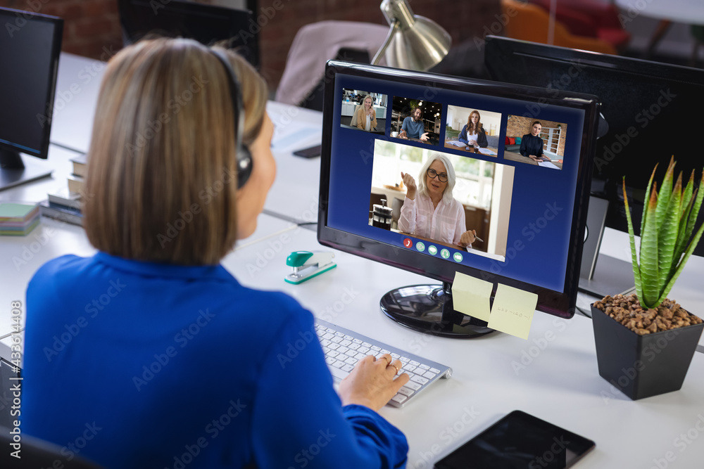 Caucasian businesswoman sitting at desk using computer having video call with group of colleagues Caucasian businesswoman sitting at desk using computer having video call with group of colleagues
