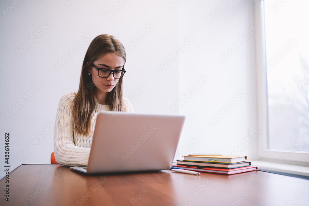 Serious young lady browsing computer while working in light workspace Serious young lady browsing computer while working in light workspace